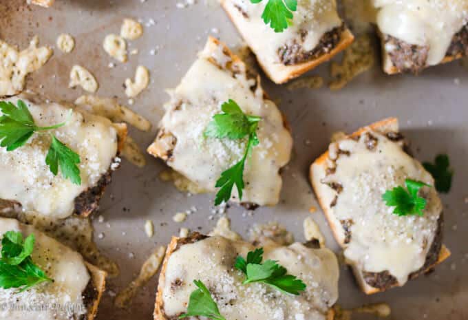 Mushroom pesto toasts with cheese and parsley on baking sheet