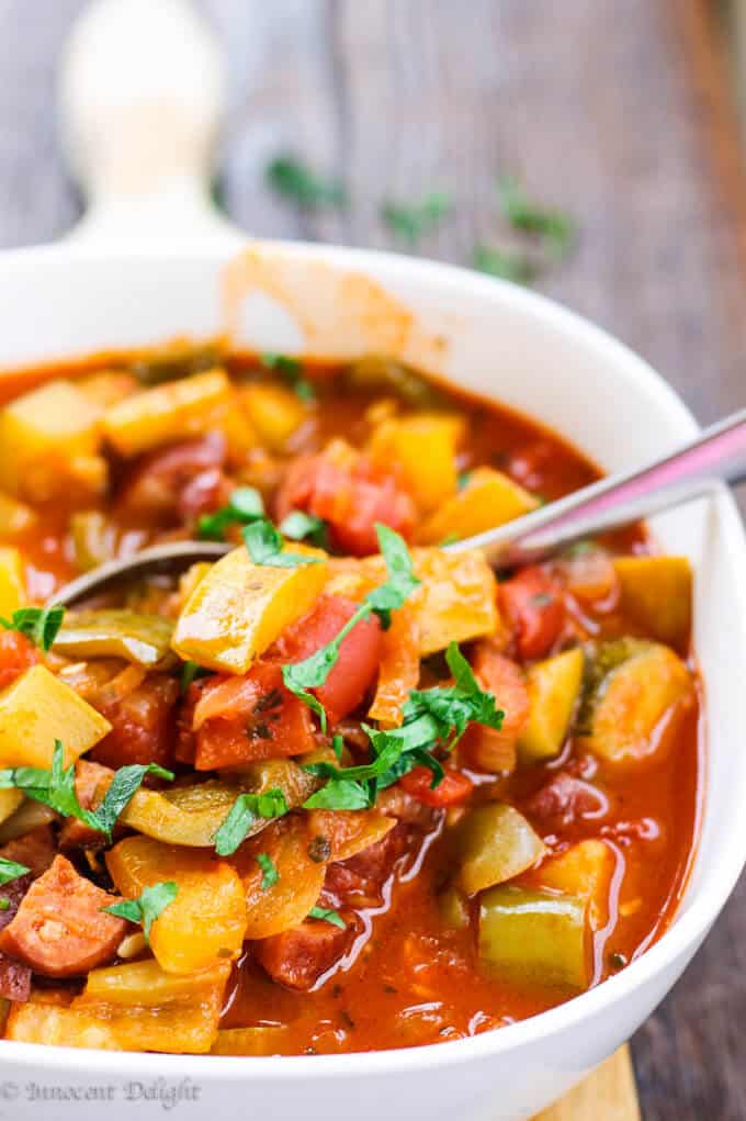 Hungarian Lecho (Tomato and Pepper Stew with Zucchini and Sausage) in a white bowl with spoon.