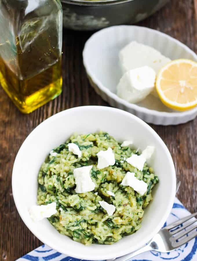 Greek Spinach Rice (Spanakorizo) with Feta cheese in a white bowl with lemon and olive oil on a side to serve it with.