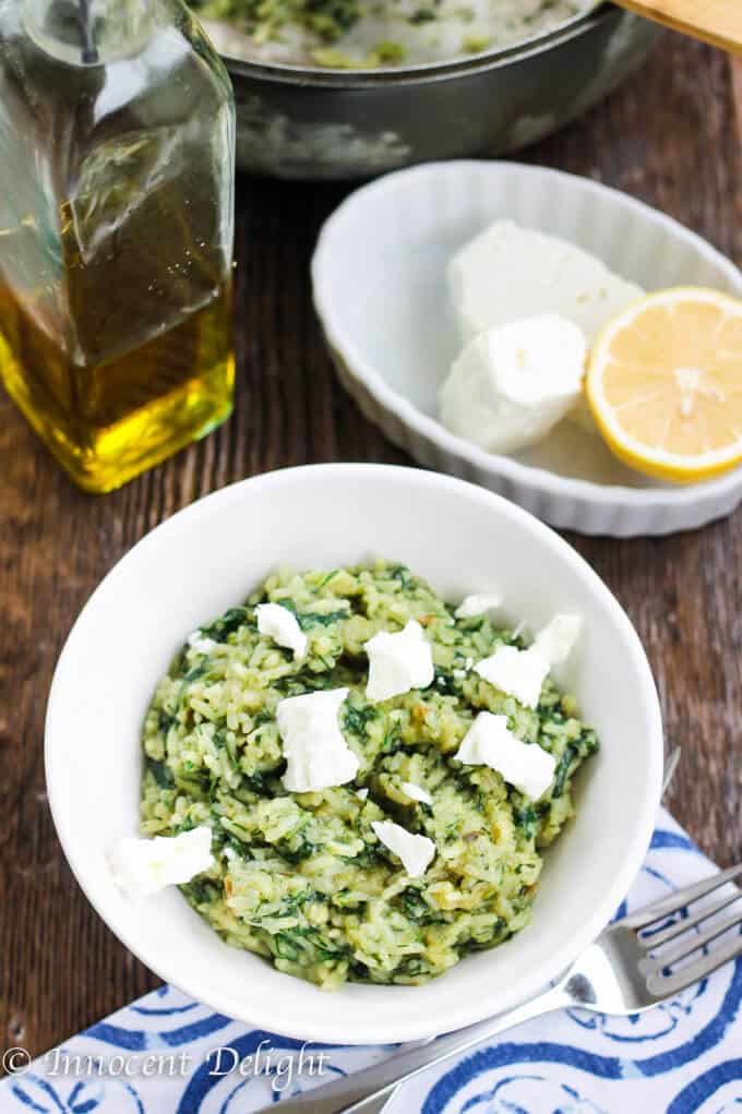 Greek Spinach Rice (Spanakorizo) with Feta cheese in a white bowl with lemon and olive oil on a side to serve it with.