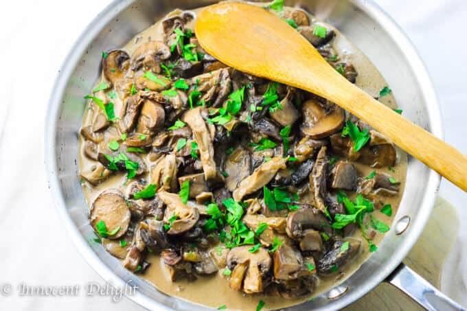 Creamy Mushroom Sauce with wide mushrooms in a pan with wooden spoon. 