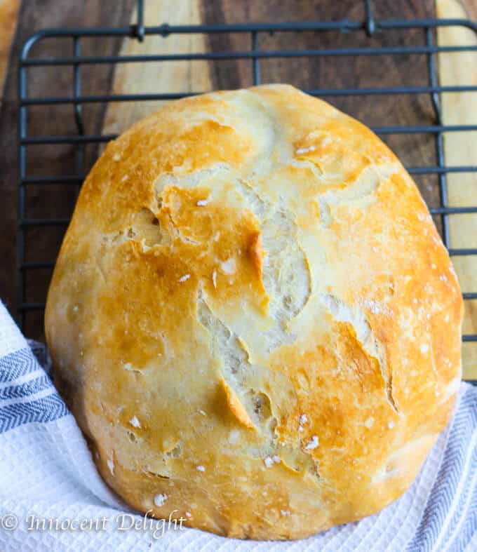 Homemade Dutch Oven Crusty Bread on a sheet rack with kitchen towel