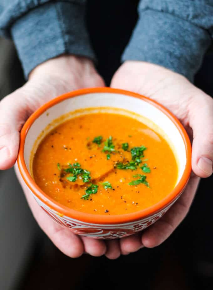 Hands holding Tomatoes Red Lentils Coconut Soup in orange bowl