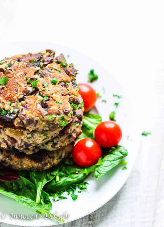 Stock of homemade veggie burgers on a white plate on white board, with spinach and tomatoes on a side