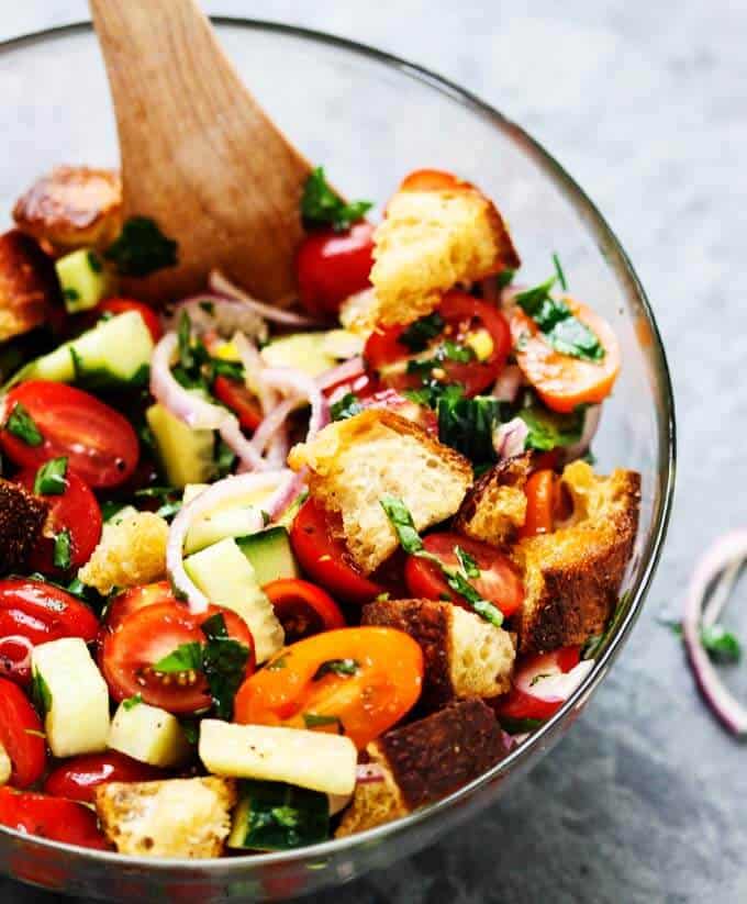 Italian Bread Salad with tomatoes, onions and cucumbers in a bowl with wooden spoon. 