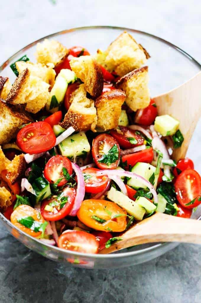 Panzanella Salad in a glass bowl with two wooden spoons. 