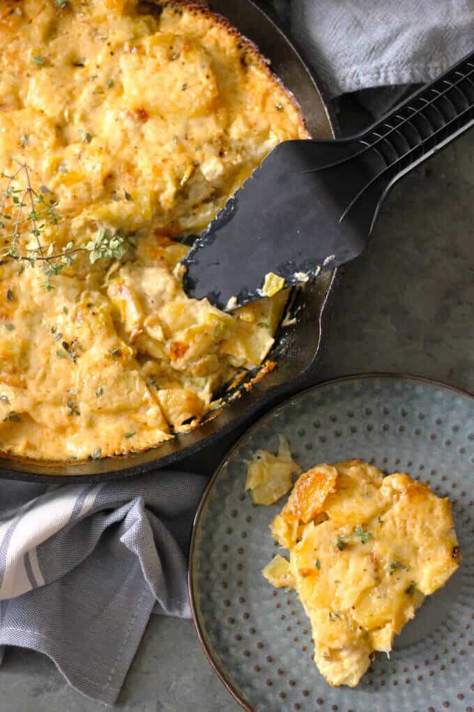 Potato Leek Casserole in a skillet with plate on a side - ultimate comfort food side dish that resembles in taste famous Potato Leek Soup; topped with cream and Gruyer Cheese, rich, decadent, elegant and delicious casserole