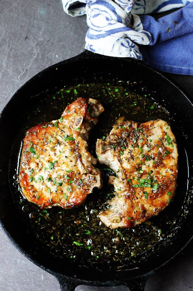 2 bone-in pork chops with garlic and herbs in a cast iron skillet with towel over handle