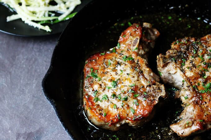 Bone-in brown sugar pork chops with garlic and herbs in a skillet