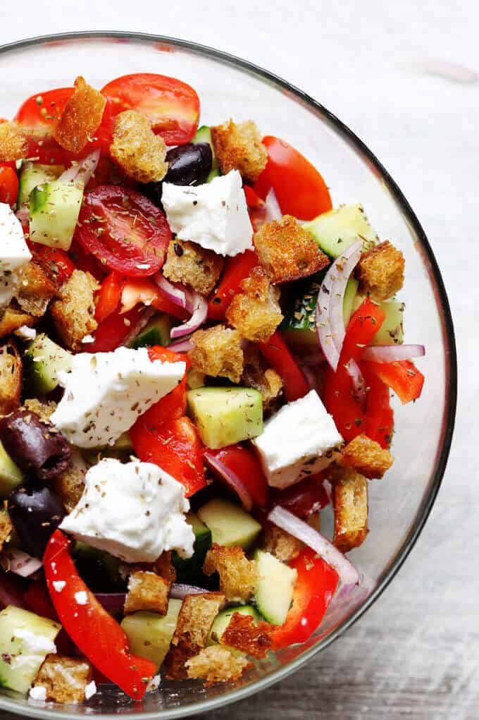 Greek Panzanella Salad with tomatoes, peppers, cucumbers, olives, feta and bread cubes in a glass bowl