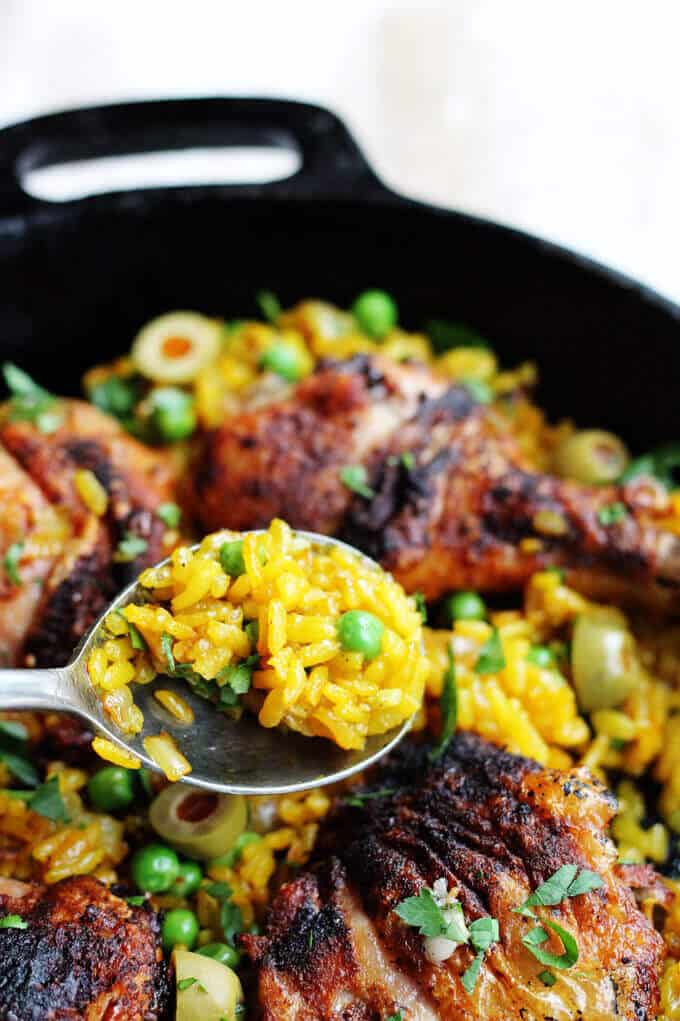 One pot chicken saffron rice with saffron, peas, olives and smoked paprika in a skillet with a spoon