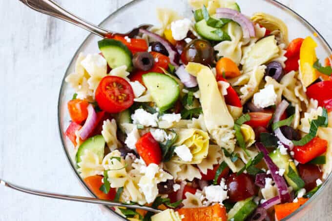 Farfalle Pasta Salad Mediterranean Style in a glass bowl with two spoons. 