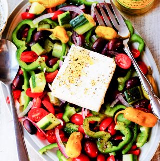 Horiatiki Greek Salad on a plate with jar of peppers on a side