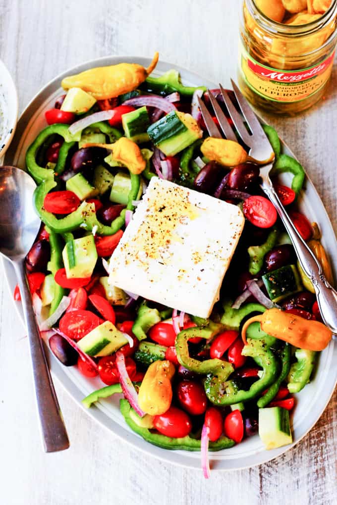 Horiatiki Salad on a plate with jar of peppers on a side