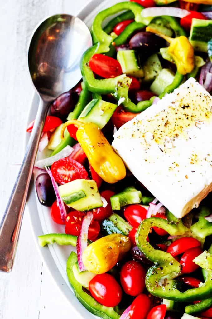 Greek Horiatiki Salad on a plate with block of feta and a spoon