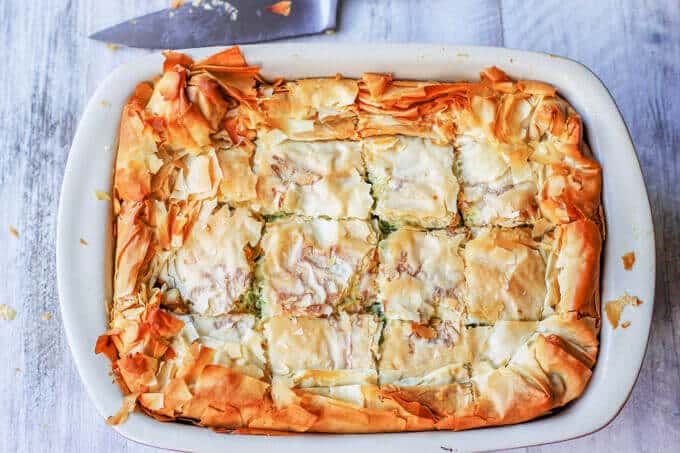 Kolokithopita zucchini pie in a casserole dish with knife next to the dish, horizontal shot