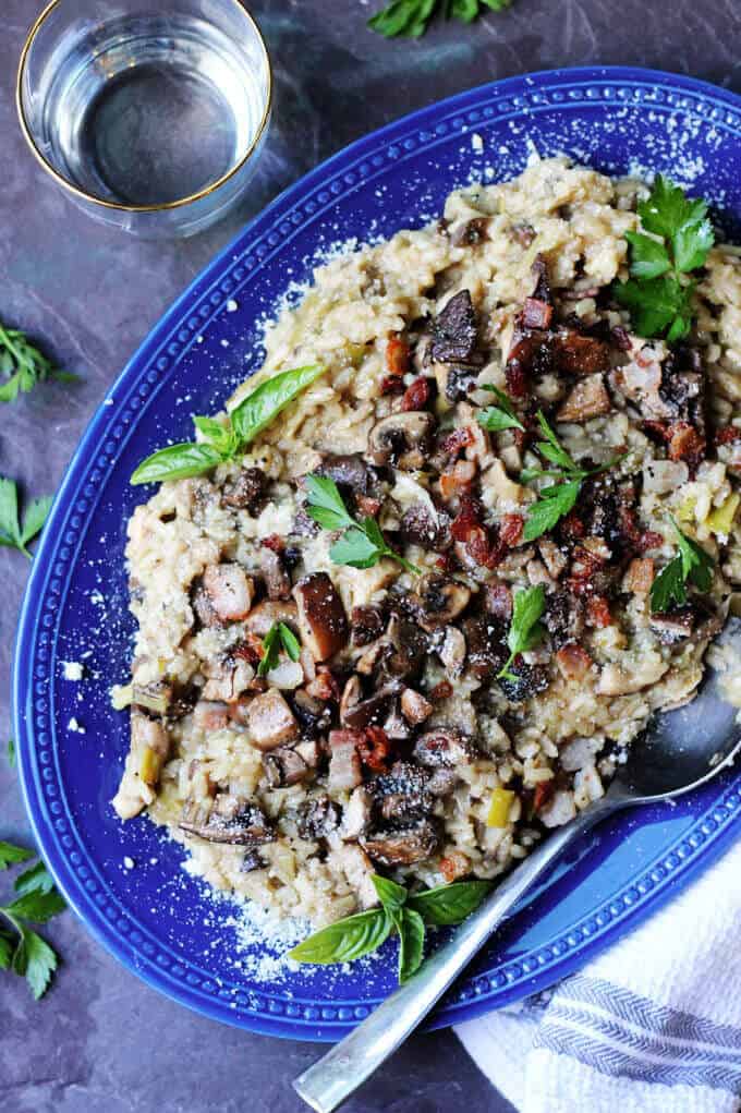 Mushroom Risotto With Bacon on a blue plate with glass of water on a side