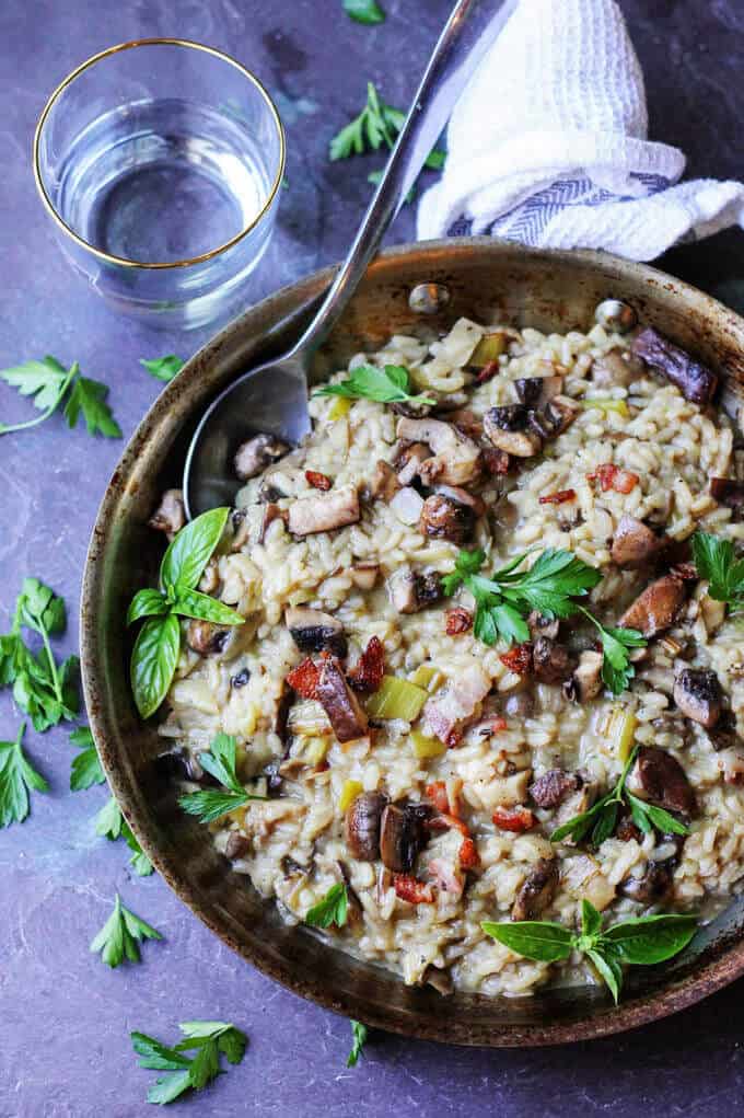 Wild Mushroom Risotto with Bacon and Leeks in a skillet with spoon and water on a side