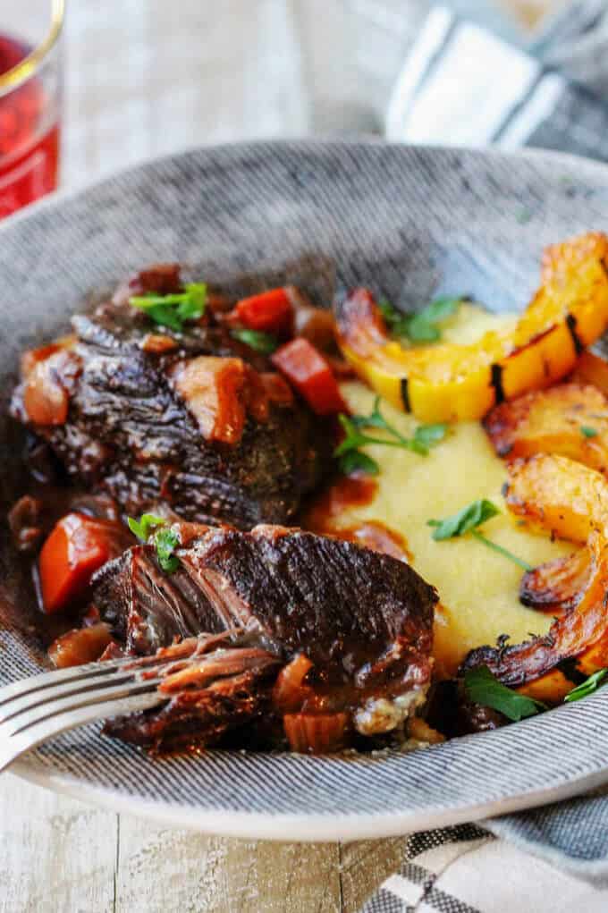 Red wine braised short ribs with parmesan polenta and delicata squash on a plate with a fork