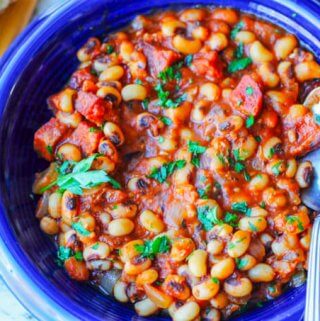 close up photo of beans with sausage and tomatoes on a blue plate with spoon, horizontal