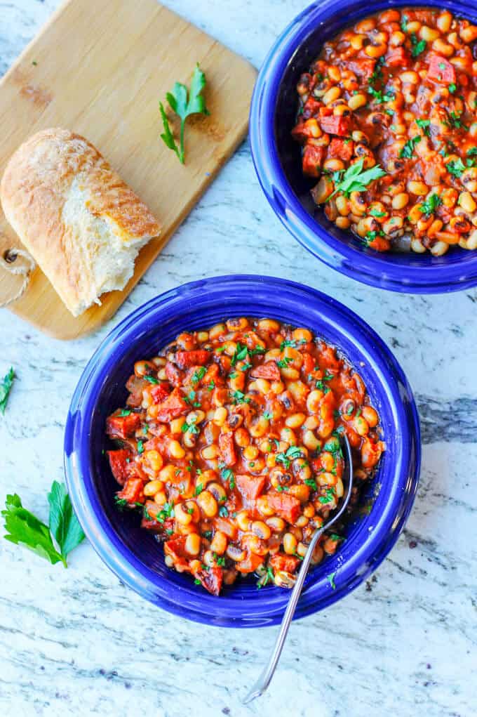 Two blue plates with breton beans, sausage and tomatoes; piece of bread on a cutting board