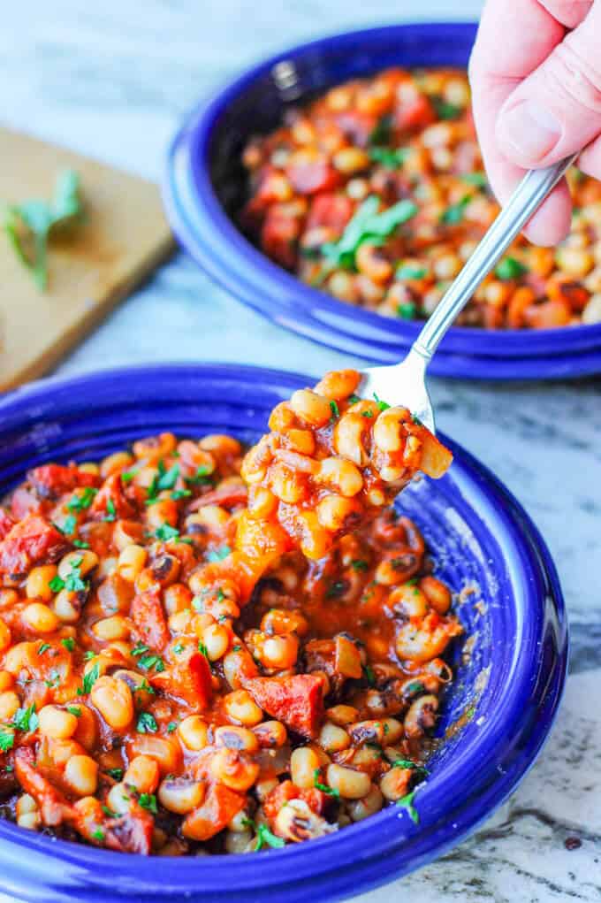 two plates with breton beans, sausage and tomato sauce with hand holding spoon with beans