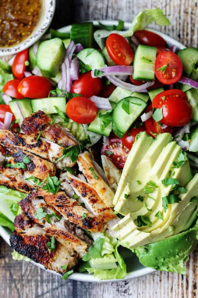 Garlic Lemon Chicken Salad on a plate with lettuce, tomatoes, cucumbers, onions, avocado