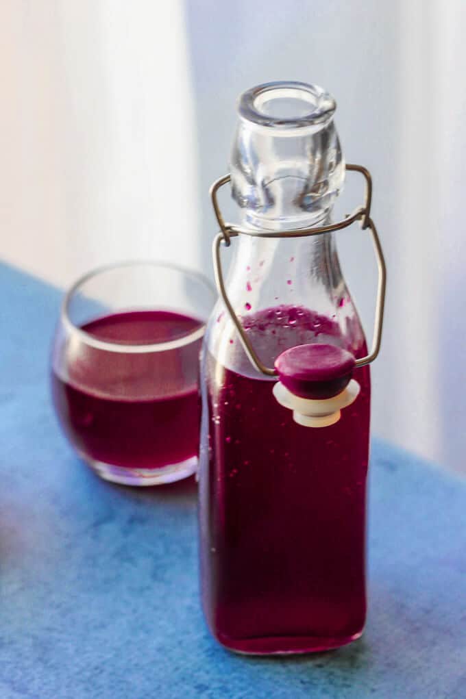 How to make beet kvass - bottle on left side and glass with beet kvass on blue background