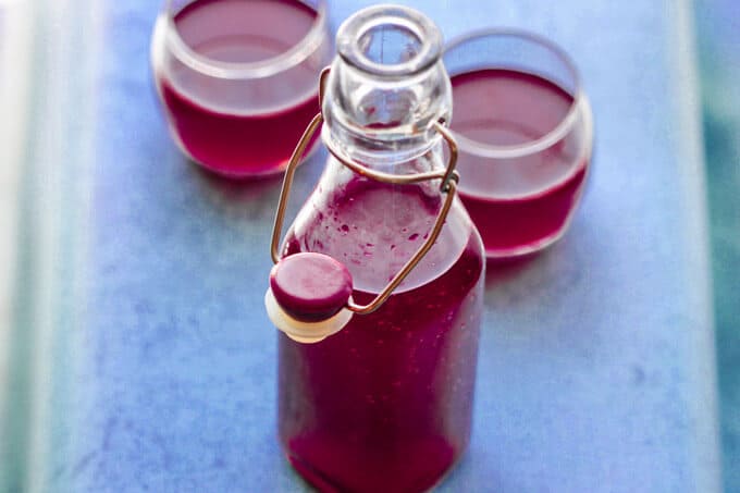 How to make beet kvass - bottle and two glasses with beet kvass ion blue background, vertical
