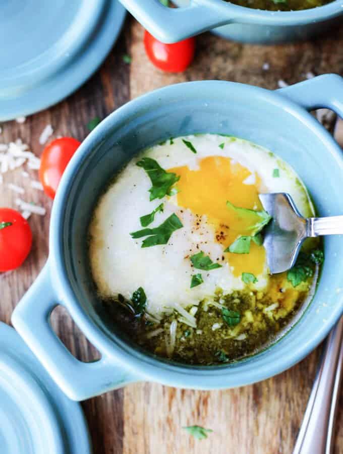 Baked eggs with tomatoes and pesto in blue ramekin with fork breaking the yolk.