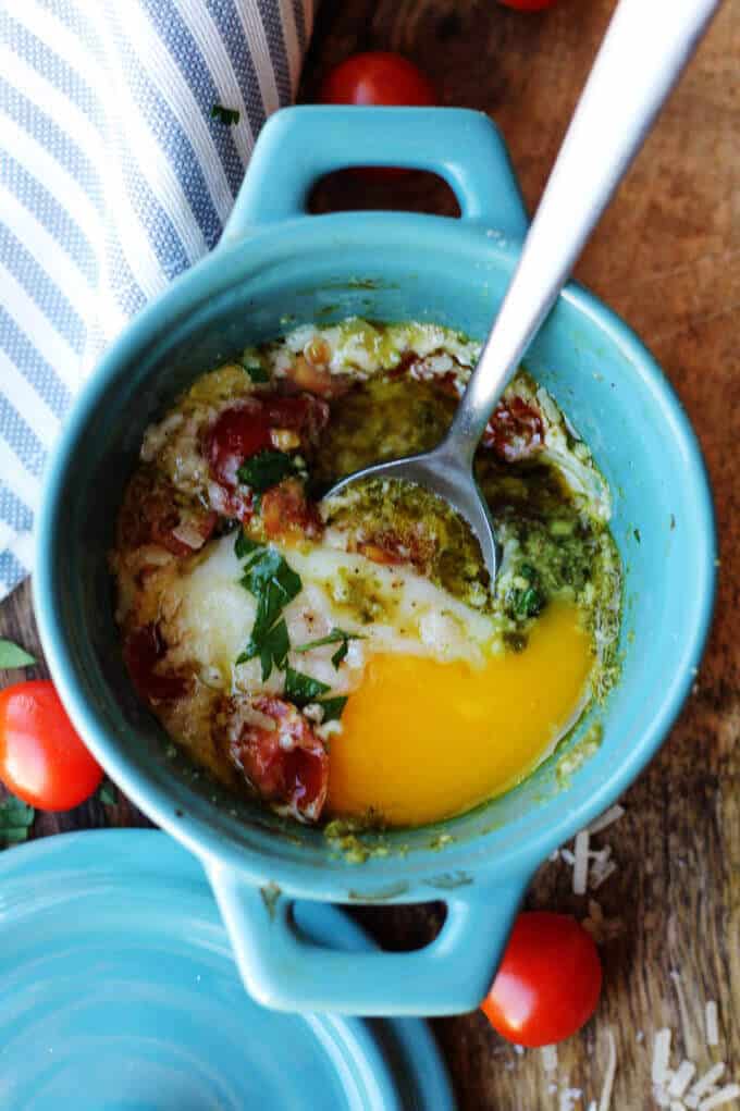baked eggs with tomatoes and pesto with spoon inside the ramekin