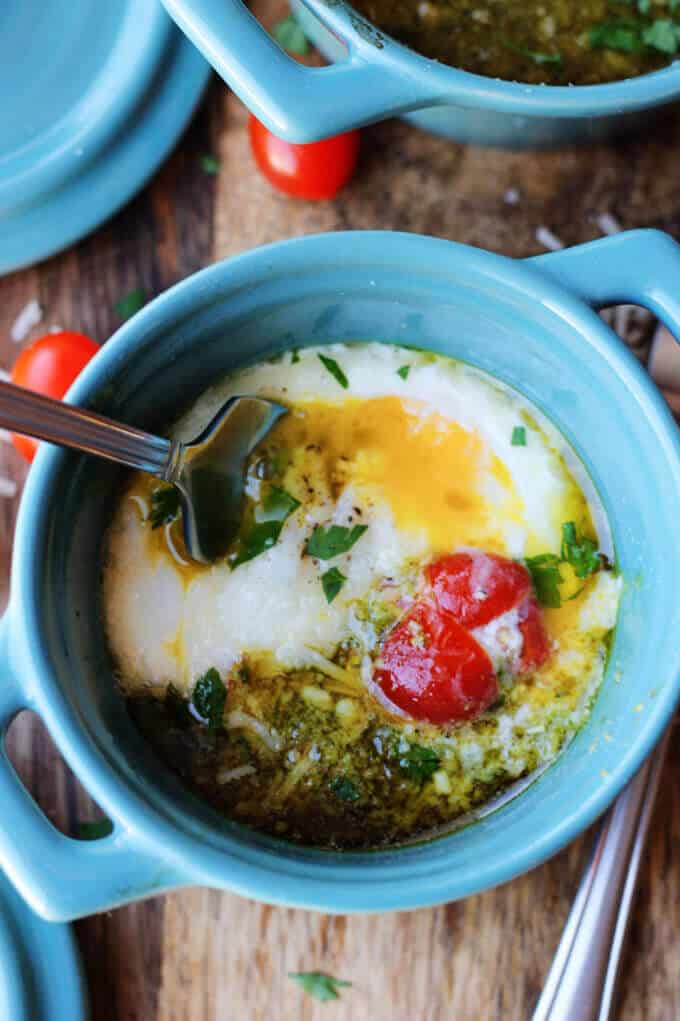 Baked eggs with tomatoes and pesto in blue ramekin with fork inside