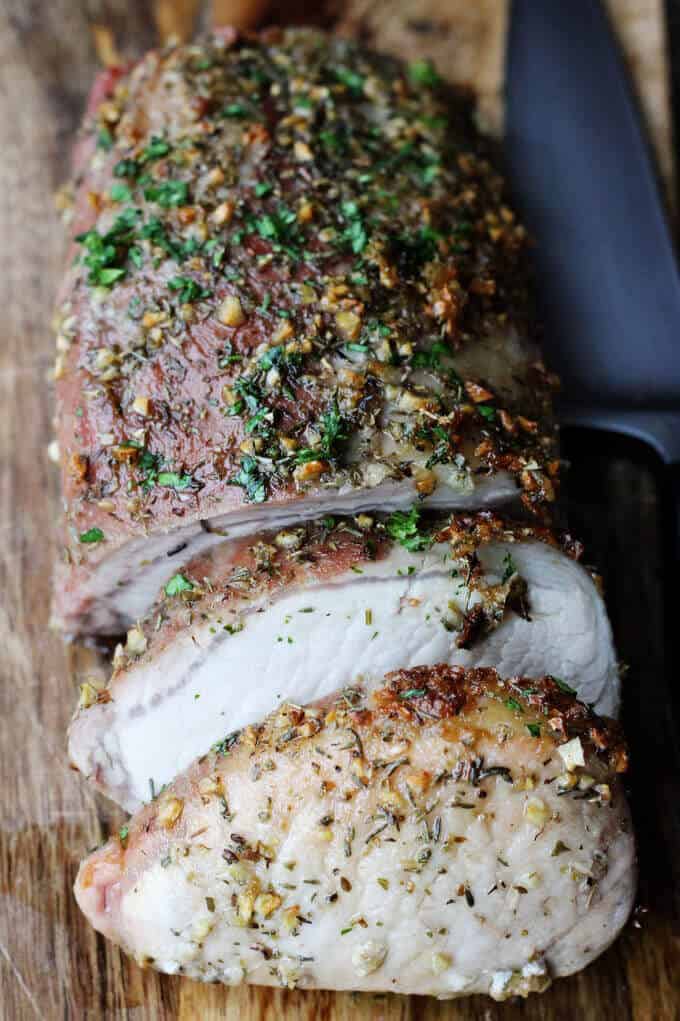 Brown Sugar Pork Loin with Garlic and Herbs on cutting board, partially sliced and knife on a side