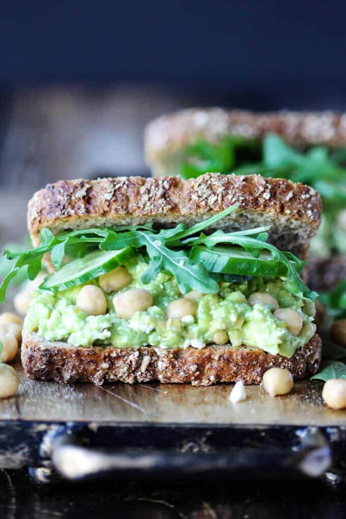 Smashed Chickpea Avocado Feta Sandwich with cucumber and arugula on a board
