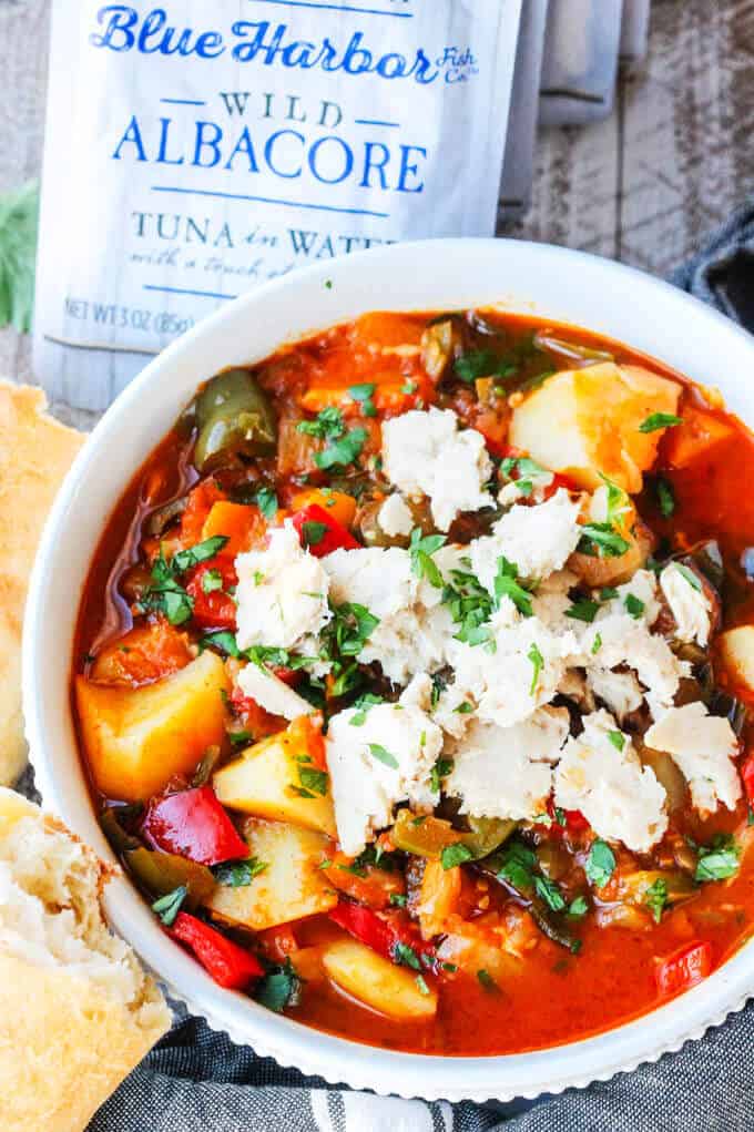 Spanish style tuna stew in a white bowl with bread on a side with tuna pouch at the back