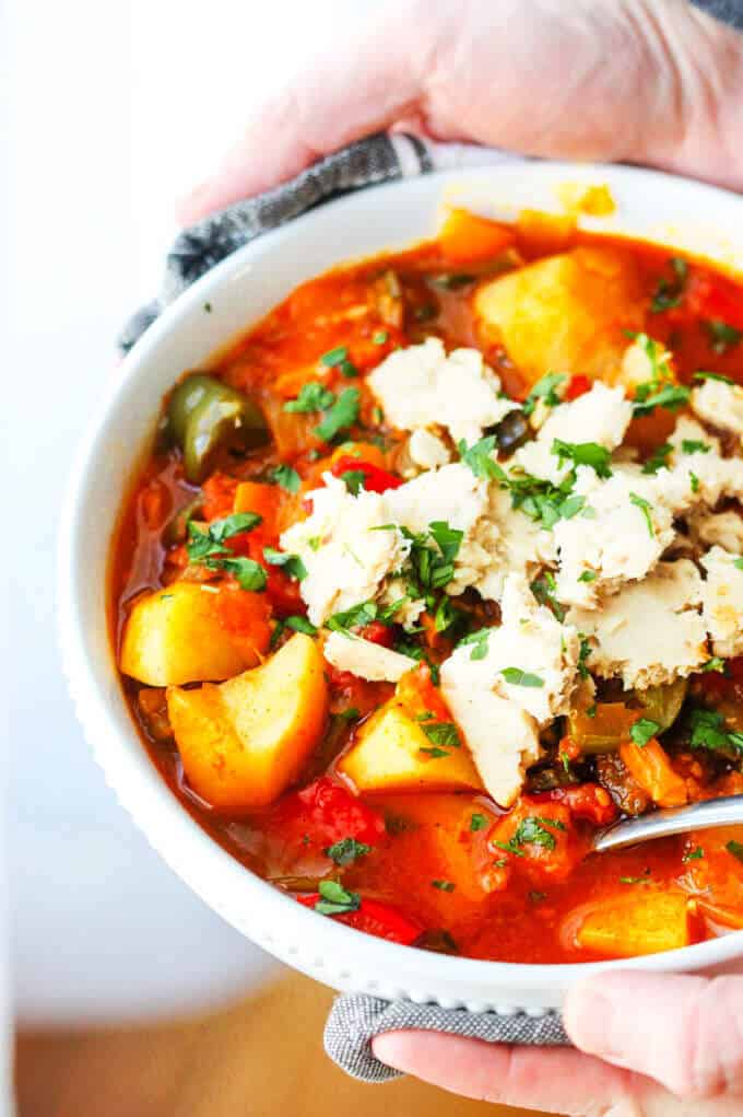 hands holding a white bowl with spanish style tuna stew