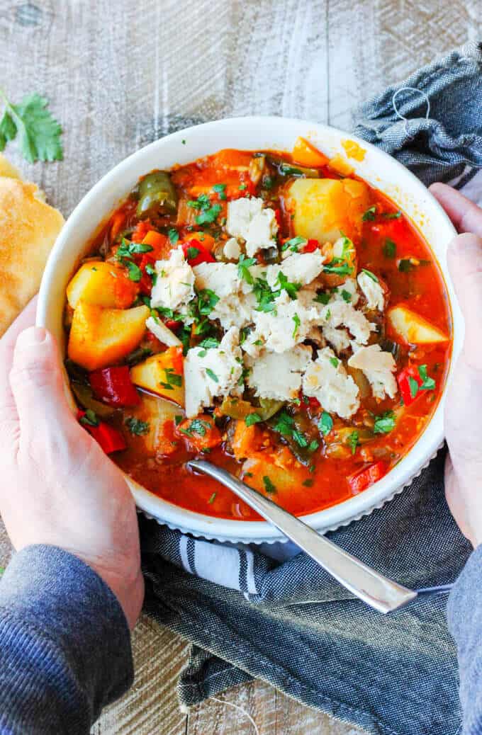 spanish style tuna stew in a whit bowl. held by man's hands with bread on a side 