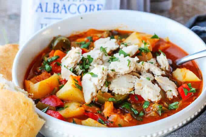 Spanish style tuna stew in a white bowl with spoon and bread on a side