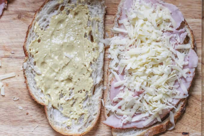 Zwei Scheiben Brot, eine mit Senf, die andere mit Schinken und geriebenem Käse