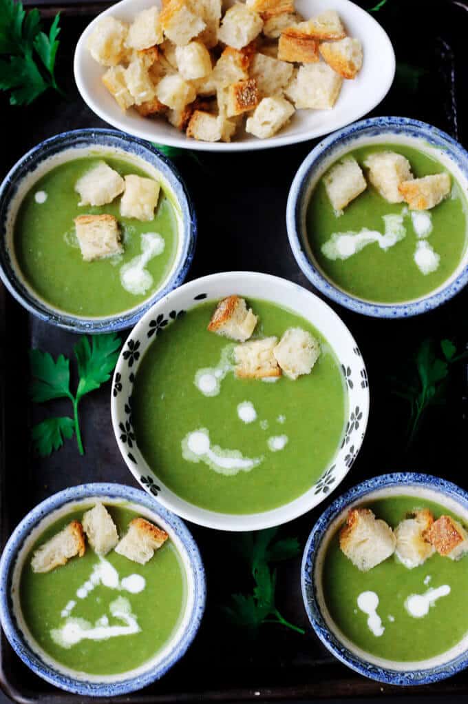healthy creamy spinach soup in 5 bowls with croutons on a side and in the soups