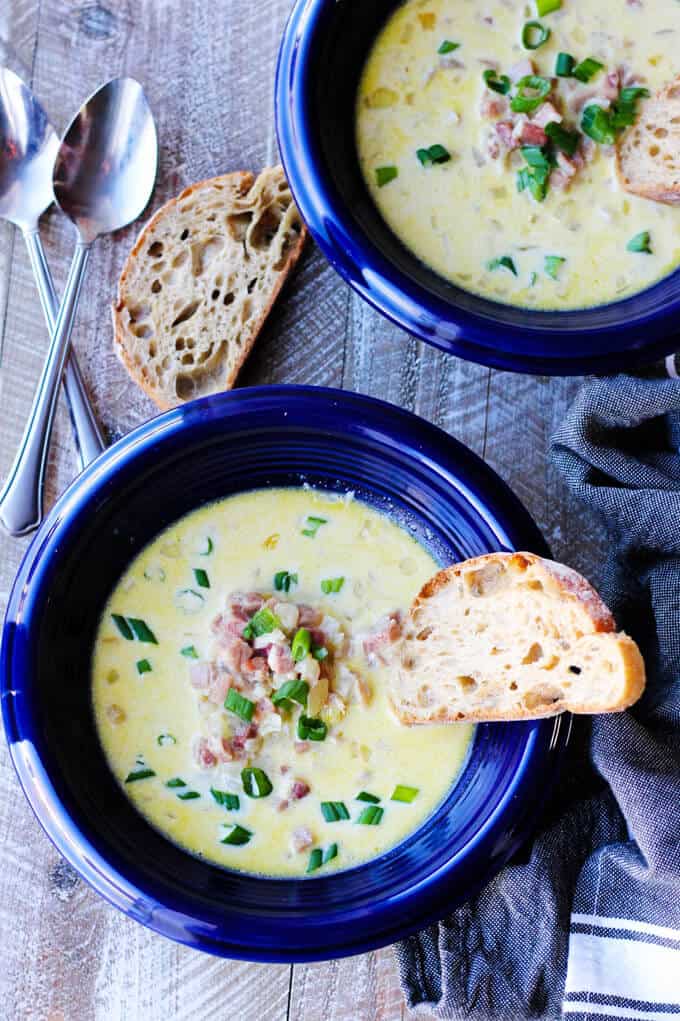 Ham and cheese soup made with white wine in blue bowls with toast inside and spoons on a side, overhead shot
