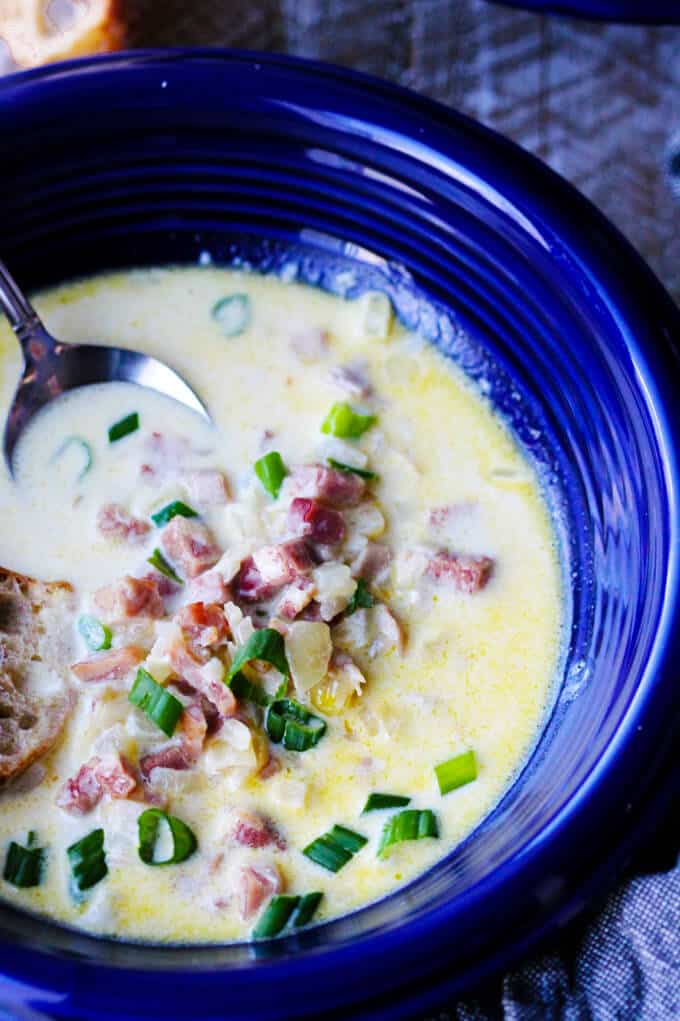 ham and cheese soup with scallion in a blue bowl with spoon sided, close up shot