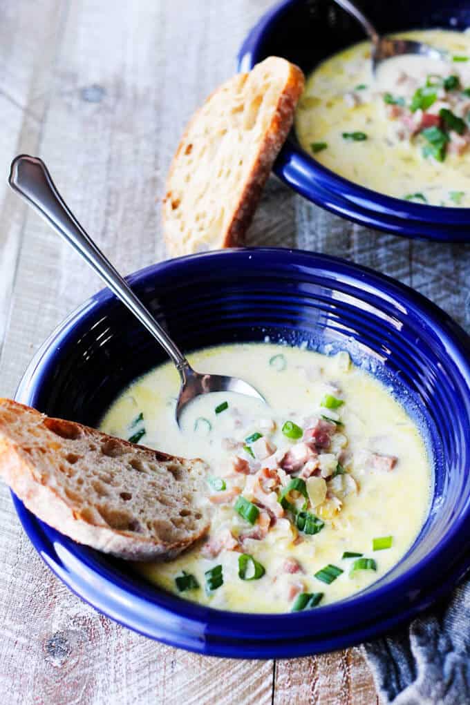 ham and cheese soup in blue bowls with scallions and bread and spoon in the bowl 