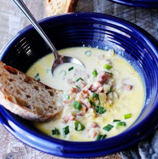 ham and cheese soup in blue bowl with scallion, bread and spoon inside, vertical shot
