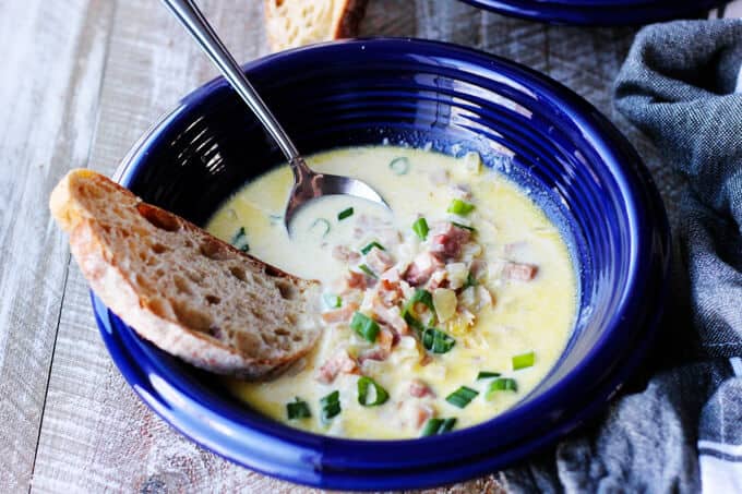 ham and cheese soup in blue bowl with scallion, bread and spoon inside, vertical shot