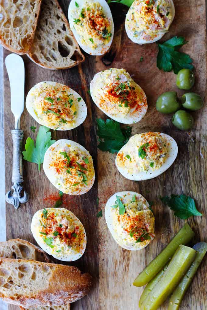 stuffed eggs on a board with bread, olives, pickles, bread on a side