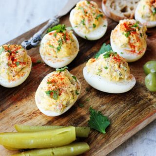 stuffed eggs on a board with bread, olives and pickles, diagonal lay out