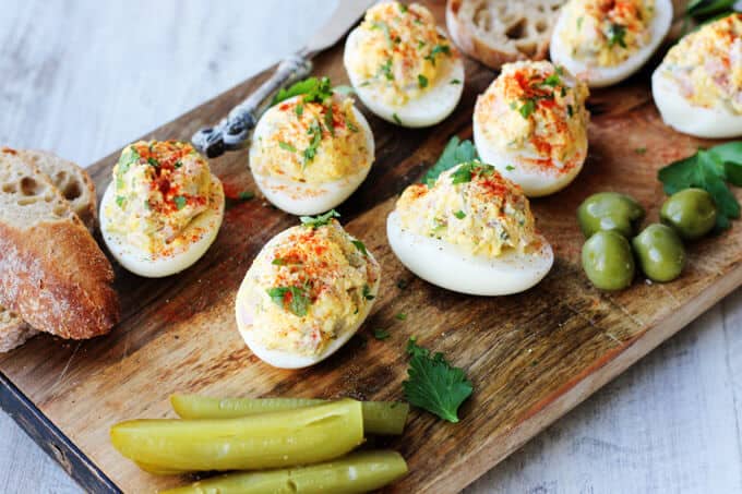 stuffed eggs on a board with bread, olives and pickles, diagonal lay out