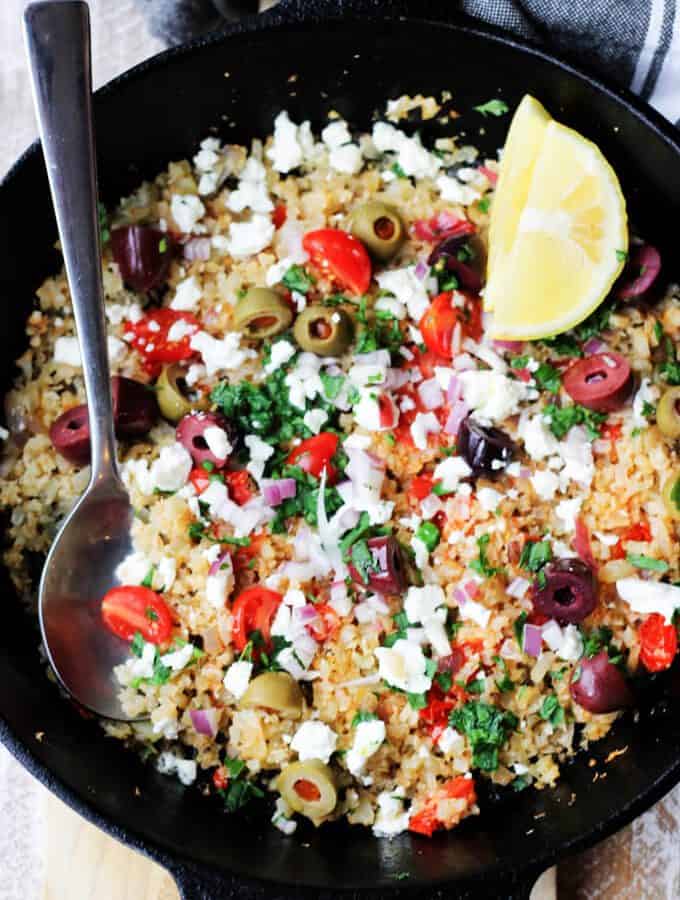Cauliflower Fried Rice in a skillet with olives, feta, lemon and spoon