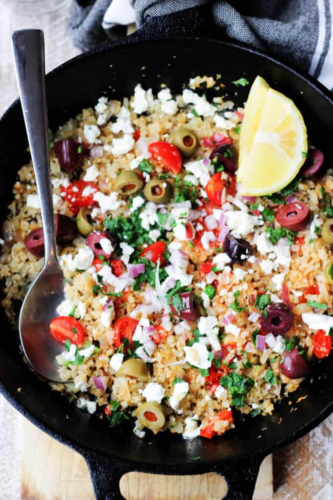 Cauliflower Fried Rice in a skillet with olives, feta, lemon and spoon
